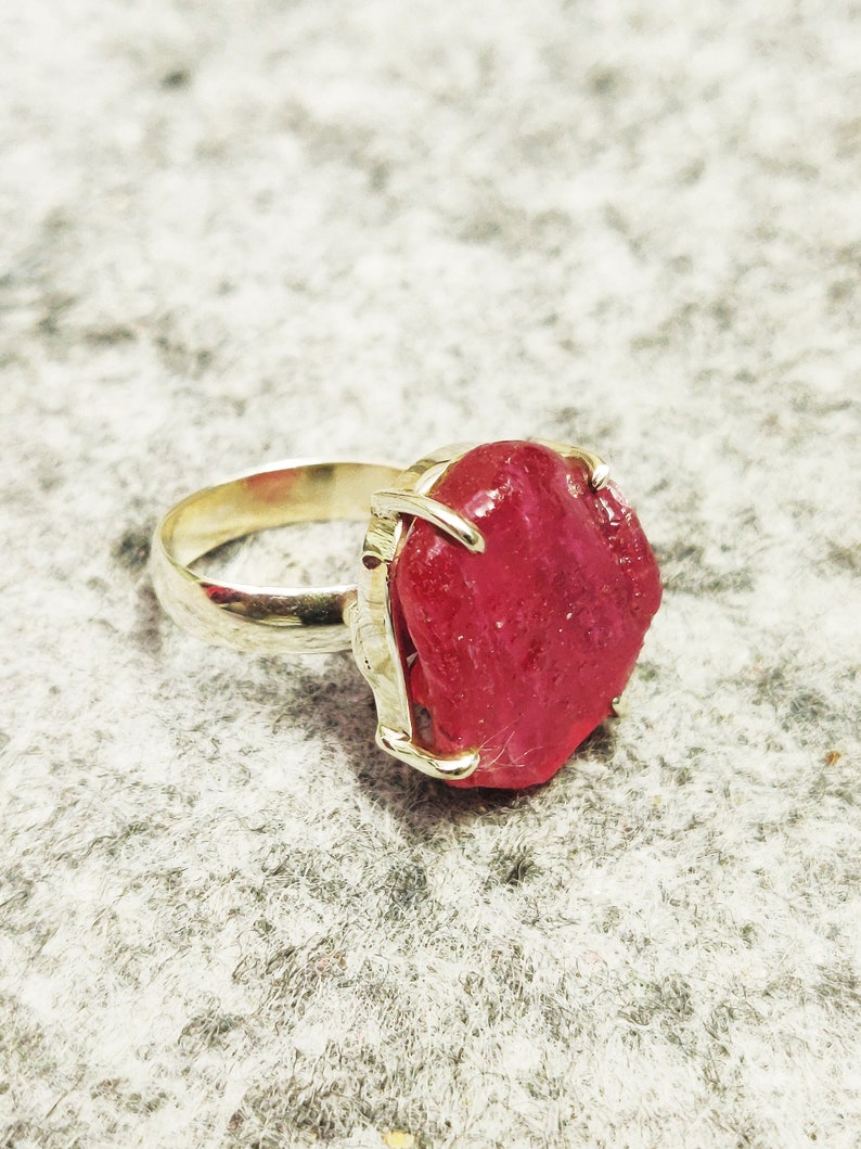 Pode incluir: Um anel de prata com uma grande gema rosa brilhante, cortada em bruto.