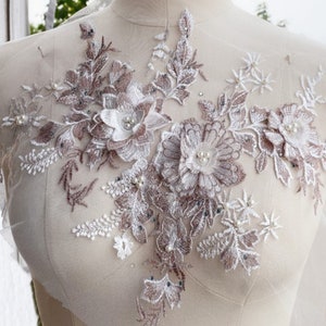 May include: A delicate floral lace applique with a blush and white color scheme. The applique features intricate floral designs with pearl embellishments.