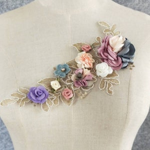 May include: A delicate floral applique with a variety of colors, including pink, purple, blue, and white. The applique features a variety of flowers and leaves, all made of fabric and lace. The applique is perfect for adding a touch of elegance to any garment or project.