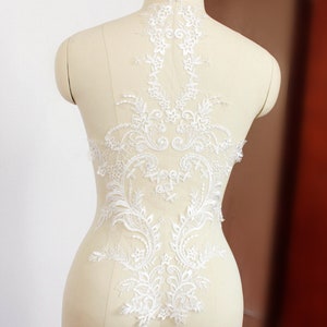 May include: White lace applique with a floral design. The lace is delicate and intricate, with a variety of floral motifs. It would be perfect for adding a touch of elegance to a wedding dress or other special occasion garment.