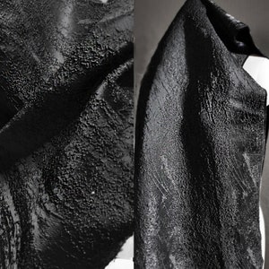 May include: Black fabric with a textured, bumpy surface. The fabric is folded and draped, showing the texture from different angles.