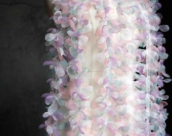 May include: A delicate, floral-inspired fabric draped over a mannequin. The fabric features layered, petal-like shapes in soft pastel colors of pink, lavender, and pale green. The design is airy and light, suggesting a decorative or apparel application.