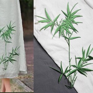 May include: A light green dress with an embroidered bamboo design. The bamboo is green and has long, slender leaves. The dress is made of a lightweight fabric and has a simple, elegant design. The bamboo design is also seen on a white fabric.