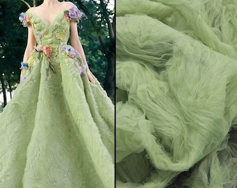 May include: A green tulle fabric with a textured, crinkled appearance. The fabric is draped and folded, showcasing its soft and delicate texture.