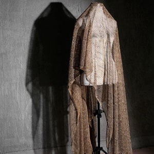 May include: A gold mesh fabric draped over a mannequin. The fabric has a shimmery, metallic finish.