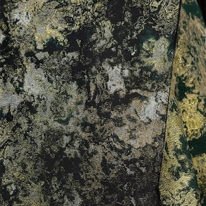 May include: Close-up of a textured fabric with a marbled design. The fabric features a mix of black, gold, silver, and green hues, creating a luxurious and abstract pattern. The material appears to be used for apparel or home decor.