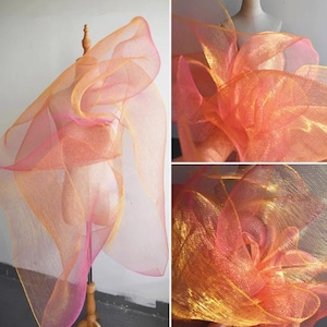 Puede incluir: Una tela transparente y en capas en tonos rosa, naranja y amarillo está drapeada sobre un maniquí. La tela parece ser una malla fina o red, creando un efecto delicado y aireado. Los colores se mezclan y se transforman, creando un efecto degradado.