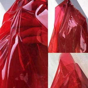 May include: Close-up of a translucent red material, possibly fabric or plastic, with light reflecting off its surface. The material is folded and draped, creating shadows and highlights. The overall effect is a vibrant, glossy texture.
