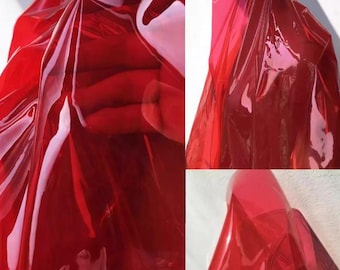 May include: A close-up of a translucent red material, possibly fabric or plastic, with light reflecting off its surface. The material is folded and draped, creating shadows and highlights. The overall effect is a vibrant, glossy texture.