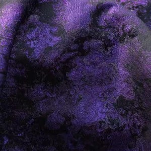 May include: Close-up of a textured fabric with a swirling pattern in shades of deep purple and black. The fabric has a shimmering, iridescent quality, with highlights catching the light. The overall effect is rich and luxurious.