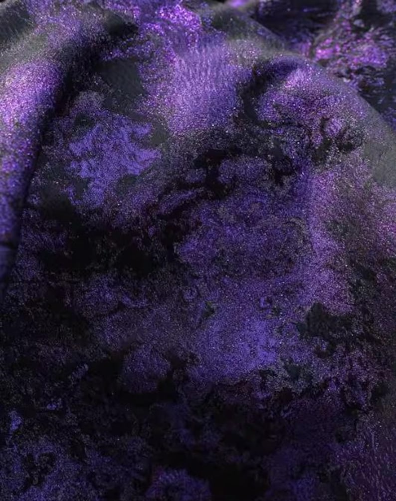 May include: Close-up of a textured fabric with a swirling pattern in shades of deep purple and black. The fabric has a shimmering, iridescent quality, with highlights catching the light. The overall effect is rich and luxurious.