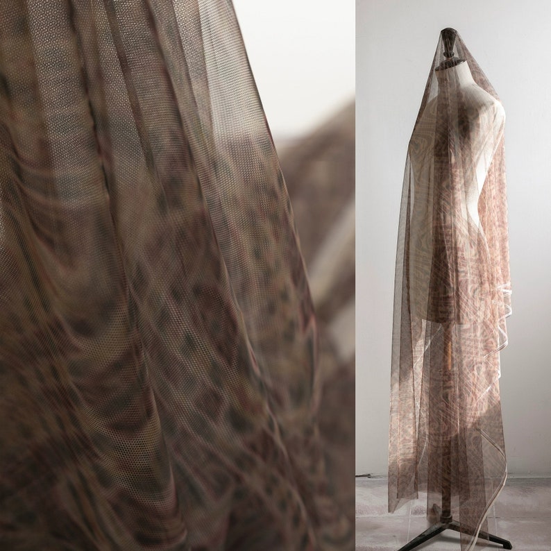 May include: A length of sheer brown fabric, patterned with a subtle design, draped over a mannequin. The fabric is semi-transparent, with a repeating pattern in brown and tan hues. The material appears lightweight and flowing, suitable for clothing or decorative use.