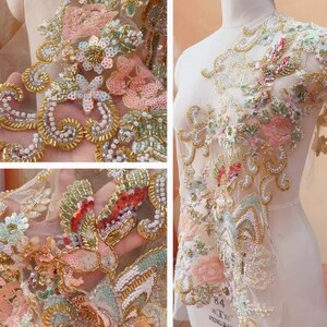 May include: Detailed shot of embroidered lace fabric with floral patterns. The design incorporates pink, gold, and green sequins and beads. The lace is displayed on a mannequin, highlighting the intricate details and craftsmanship.
