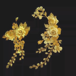 Może przedstawiać: Dwie złote naszywki z haftem kwiatowym na czarnym tle. Naszywki przedstawiają szczegółowe kwiaty, liście i łodygi z metalicznym połyskiem. Projekt jest skomplikowany i ozdobny, odpowiedni do zdobienia odzieży lub rękodzieła.