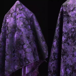 May include: A draped fabric with a marbled pattern in shades of purple and black. The fabric is folded, creating a textured surface with highlights and shadows. The material appears to be soft and flowing, suitable for apparel or home decor.