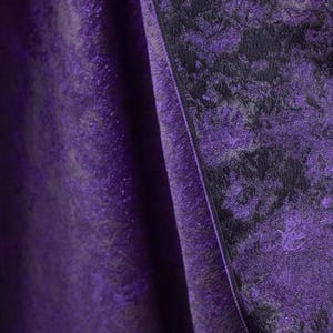 May include: Close-up of a draped fabric with a textured, shimmering surface. The fabric is a deep purple color with a darker, mottled pattern. The folds of the fabric create shadows and highlights, adding depth and dimension to the image. The overall effect is luxurious and elegant.