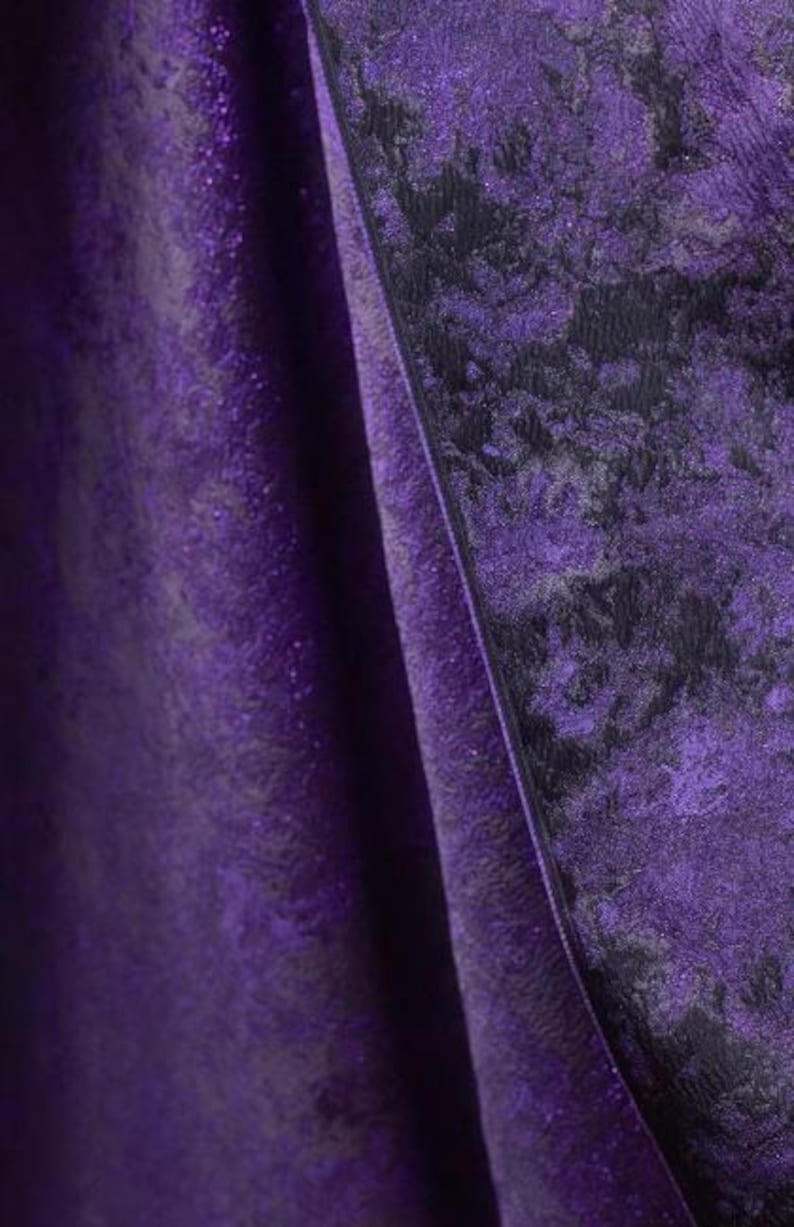 May include: Close-up of a draped fabric with a textured, shimmering surface. The fabric is a deep purple color with a darker, mottled pattern. The folds of the fabric create shadows and highlights, adding depth and dimension to the image. The overall effect is luxurious and elegant.