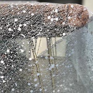 Könnte beinhalten: Weißer Tüllstoff mit einem zarten, feinen Maschenmuster und weißen Punkten. Der Stoff ist durchsichtig und hat eine weiche, fließende Textur.