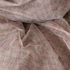 May include: Close-up of a sheer fabric with a repeating diamond pattern in shades of mauve and off-white. The fabric is draped, creating soft folds and shadows. The material appears lightweight and delicate, suitable for apparel or decorative purposes.
