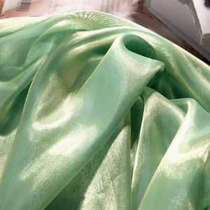Puede incluir: Primer plano de una tela transparente verde claro con un ligero brillo. La tela es suave y fluida, con una textura delicada.