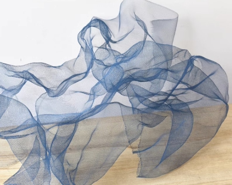 May include: A blue sheer fabric with a delicate, airy texture. The fabric is draped and folded, creating a soft, flowing shape.