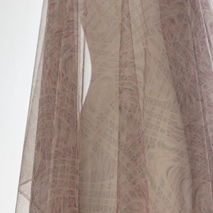 May include: A sheer fabric with a geometric pattern in pink and white hues. The fabric is draped, forming soft folds and a flowing look. The pattern is visible through the sheer material, adding depth and texture to the design.