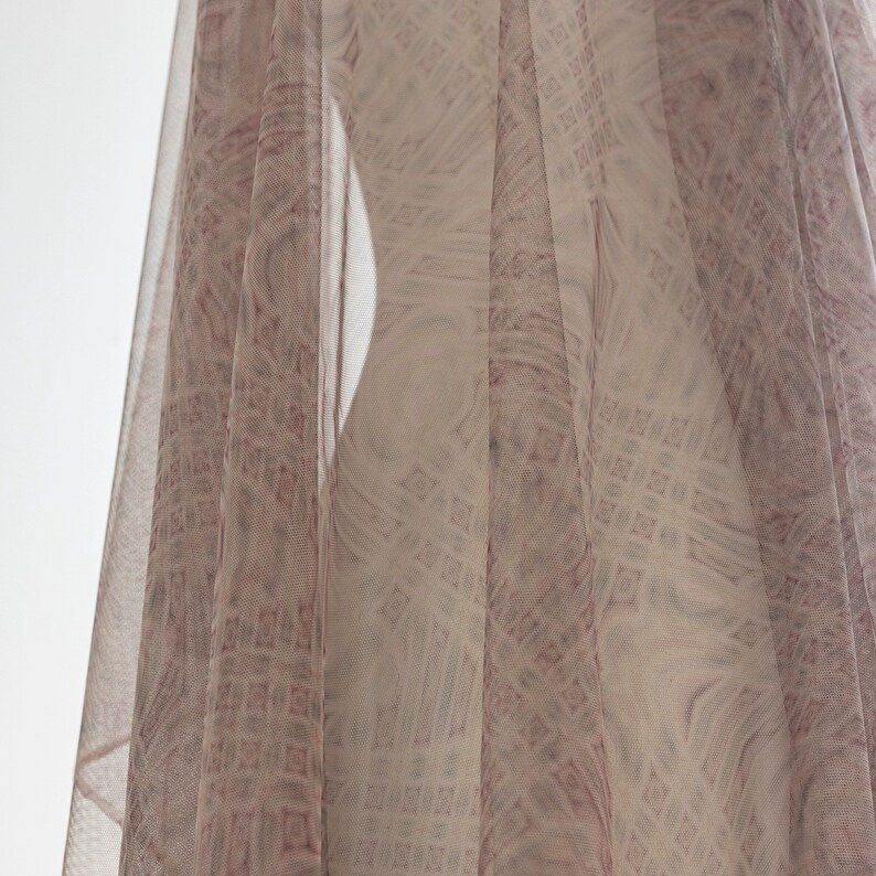 May include: A sheer fabric with a geometric pattern in pink and white hues. The fabric is draped, forming soft folds and a flowing look. The pattern is visible through the sheer material, adding depth and texture to the design.
