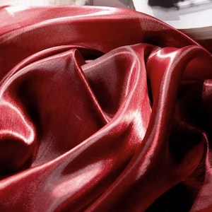 Peut inclure: Gros plan sur un tissu soyeux rouge foncé avec un léger reflet. Le tissu est drapé et plié, créant des lignes douces et fluides.