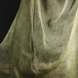 May include: A green sheer fabric with a textured pattern, draped and folded to create soft, flowing lines.