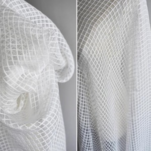 Könnte beinhalten: Weißer, durchsichtiger Stoff mit einem Gittermuster. Der Stoff ist leicht und hat eine zarte Textur.