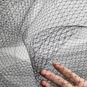 Op de afbeelding: Zwarte tule stof met een fijn, ruitvormig gaaspatroon. De stof is zacht en delicaat en is perfect voor het maken van verschillende projecten, zoals sluiers, hoofdbanden en andere accessoires.