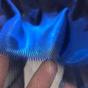 Könnte beinhalten: Nahaufnahme eines schimmernden, irisierenden blauen Stoffes. Das Material hat ein strukturiertes, geripptes Aussehen mit einem feinen Mesh-Overlay. Der Stoff reflektiert das Licht und erzeugt einen dynamischen und optisch ansprechenden Effekt. Die Gesamtästhetik ist modern und luxuriös.