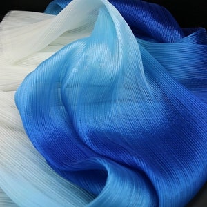 Puede incluir: Una tela de degradado de color en tonos de blanco, azul claro y azul oscuro. La tela está plisada y tiene un brillo sedoso.
