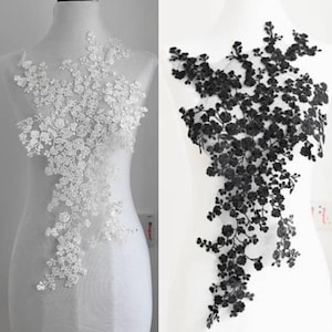 Puede incluir: Dos apliques de encaje floral, uno blanco y otro negro, expuestos sobre maniquíes. Los apliques presentan delicados y detallados diseños florales, ideales para embellecer prendas o proyectos de artesanía. El aplique blanco está a la izquierda y el negro a la derecha.