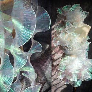May include: White iridescent ruffled fabric with a shimmery green sheen. The fabric is layered and folded to create a dramatic effect.