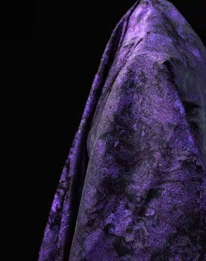 May include: A close-up of a draped fabric with a textured, marbled appearance. The fabric is primarily a deep purple color with black accents, creating a dramatic and luxurious look. The folds and shadows add depth.