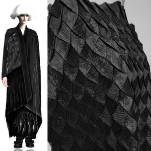 May include: A black garment with a unique, textured, scale-like design. The fabric is pleated and appears to be made of a soft material.