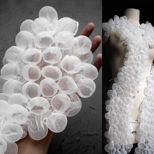 Puede incluir: Tela blanca con una textura similar a burbujas. La tela está dispuesta en forma de cascada, creando un efecto voluminoso y aireado.