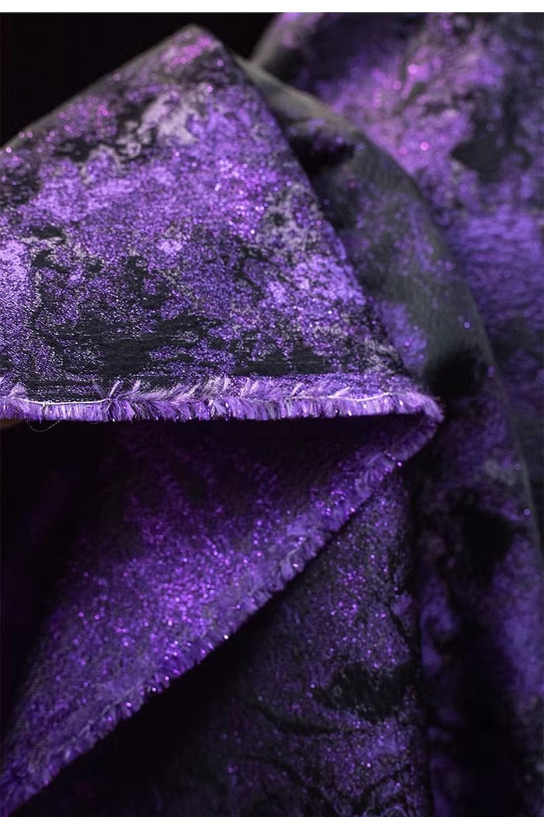 May include: Close-up of a folded fabric with a shimmering purple and black pattern. The fabric has a textured surface with a glittery effect, and the edges are frayed. The overall theme is textile and design.