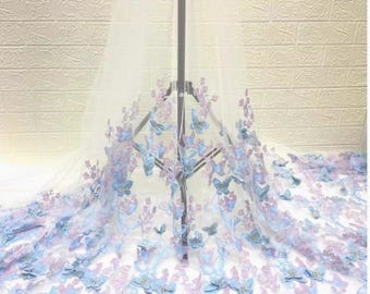 Può includere: Un tessuto bianco trasparente con un motivo a farfalle blu e lavanda. Le farfalle tridimensionali creano un aspetto stravagante ed elegante. Ideale per veli da sposa o progetti decorativi.
