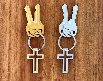 May include: Two keychains with cross charms. One keychain has gold keys and a gold cross charm. The other keychain has silver keys and a silver cross charm.