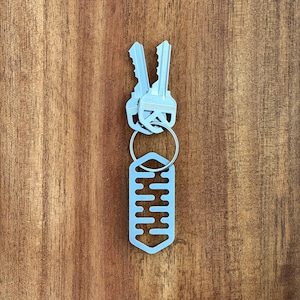 May include: A silver key chain with a key ring and two keys. The key chain has a decorative metal tag with a geometric pattern.