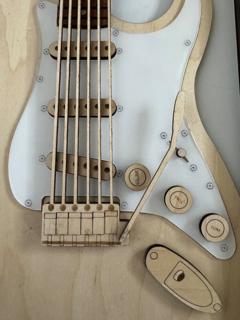 May include: Close-up of a wooden guitar body with a white pickguard. The guitar has a bridge, six strings, and three knobs labeled "Volume", "Inch", and "Tone".
