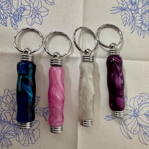 Pode incluir: Quatro chaveiros com diferentes desenhos de espiral coloridos. Os chaveiros são de metal e têm um acabamento prateado. As espirais são azuis, cor-de-rosa, brancas e roxas.