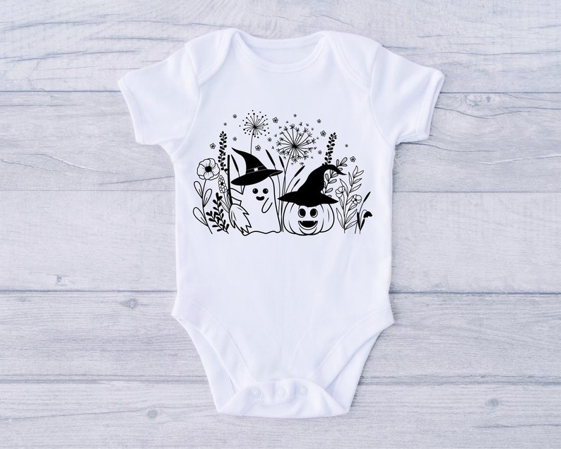 May include: White baby onesie with a black and white illustration of a ghost wearing a witch hat and a pumpkin wearing a witch hat. The ghost and pumpkin are surrounded by black and white flowers and leaves.