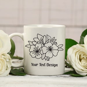 Pu&ograve; includere: Tazza in ceramica bianca con un design floreale nero e il testo "Your Text Design". La tazza &egrave; circondata da rose bianche.