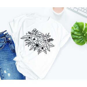 Puede incluir: Una camiseta blanca con un dibujo de l&iacute;nea negra de un ramo de flores. El ramo incluye rosas, flores m&aacute;s peque&ntilde;as y hojas.