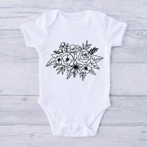 Puede incluir: Un body blanco para beb&eacute; con un dise&ntilde;o floral negro que presenta un ramo de rosas y otras flores.