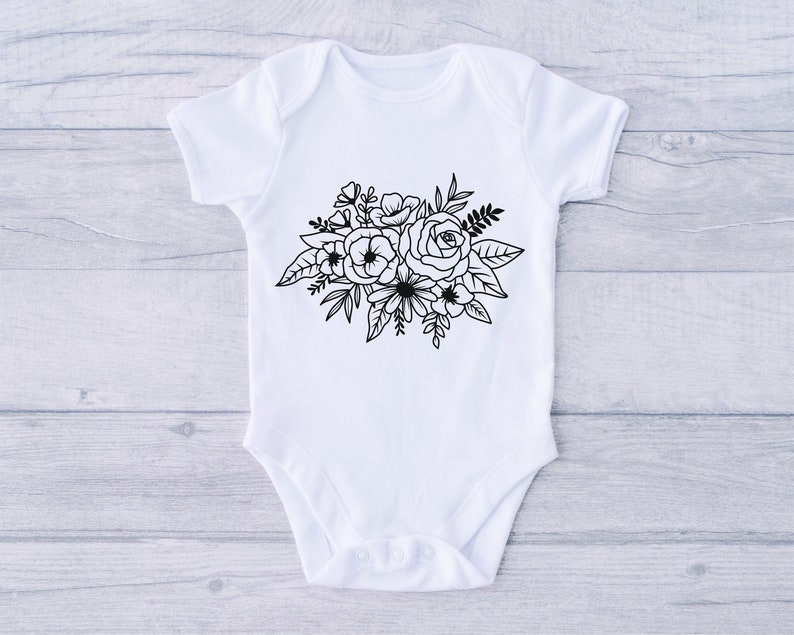 Puede incluir: Un body blanco para beb&eacute; con un dise&ntilde;o floral negro que presenta un ramo de rosas y otras flores.