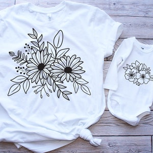 Pu&ograve; includere: Una maglietta bianca e un body bianco a maniche lunghe con un disegno floreale nero. Il disegno presenta due grandi fiori con pi&ugrave; petali e foglie.